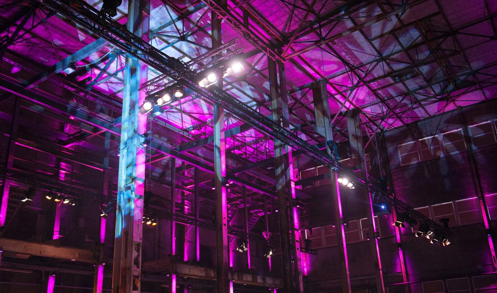 Industriehal met kleurrijk lichtspektakel en hoge plafonds, geschikt voor evenementen en feesten.