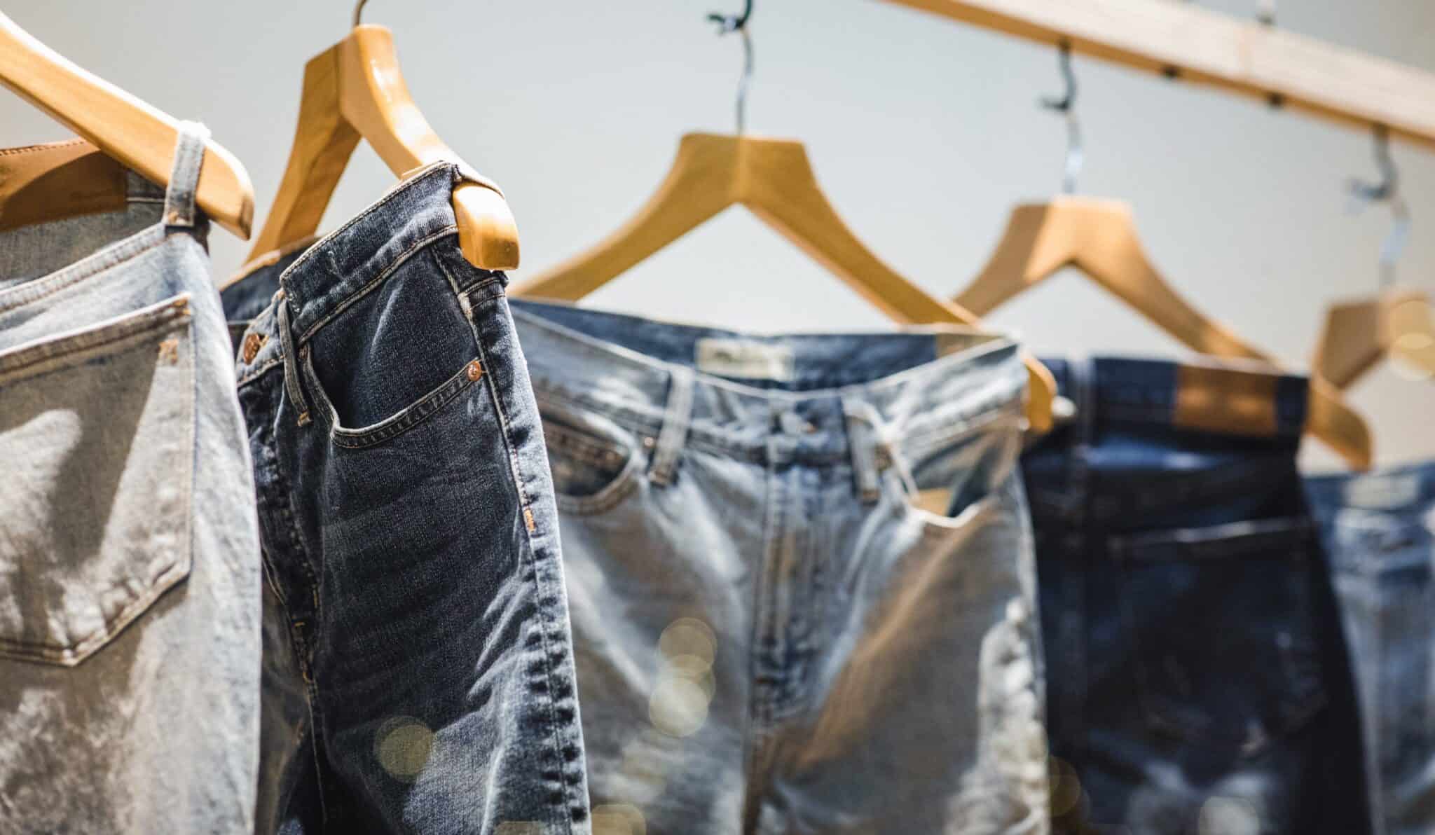 Verschillende denim jeans hangen aan houten hangers in winkel.