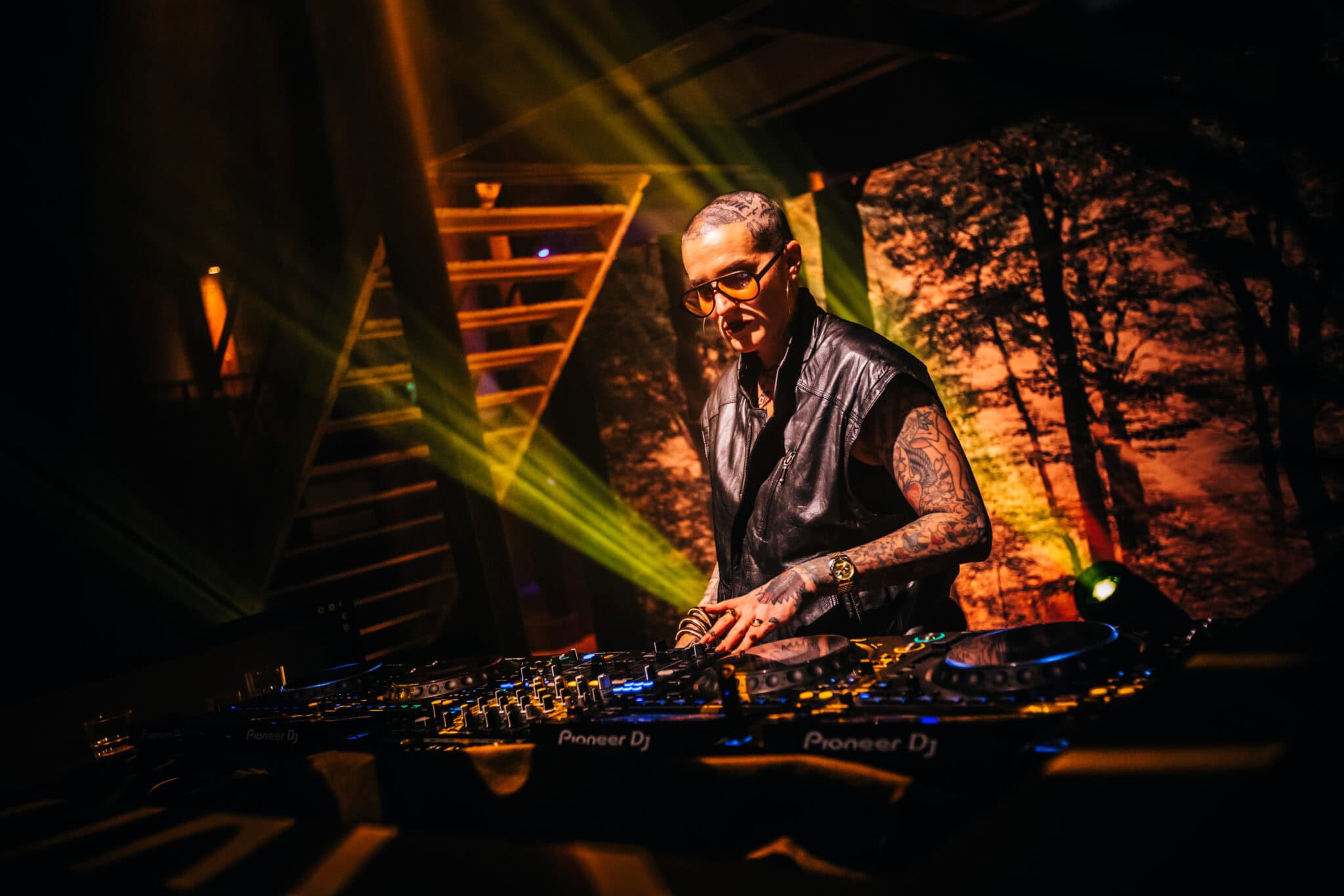 Vrouw DJ met tattoos en bril achter draaitafels tijdens optreden.