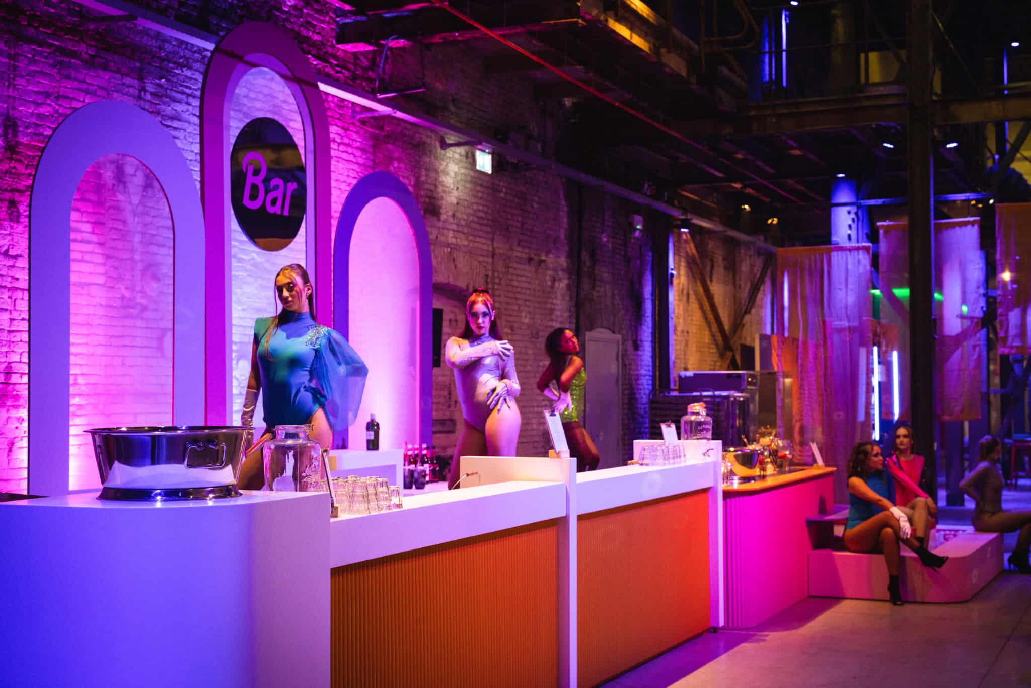 Modern bar met kleurrijke verlichting en mannequins in een industriële setting.