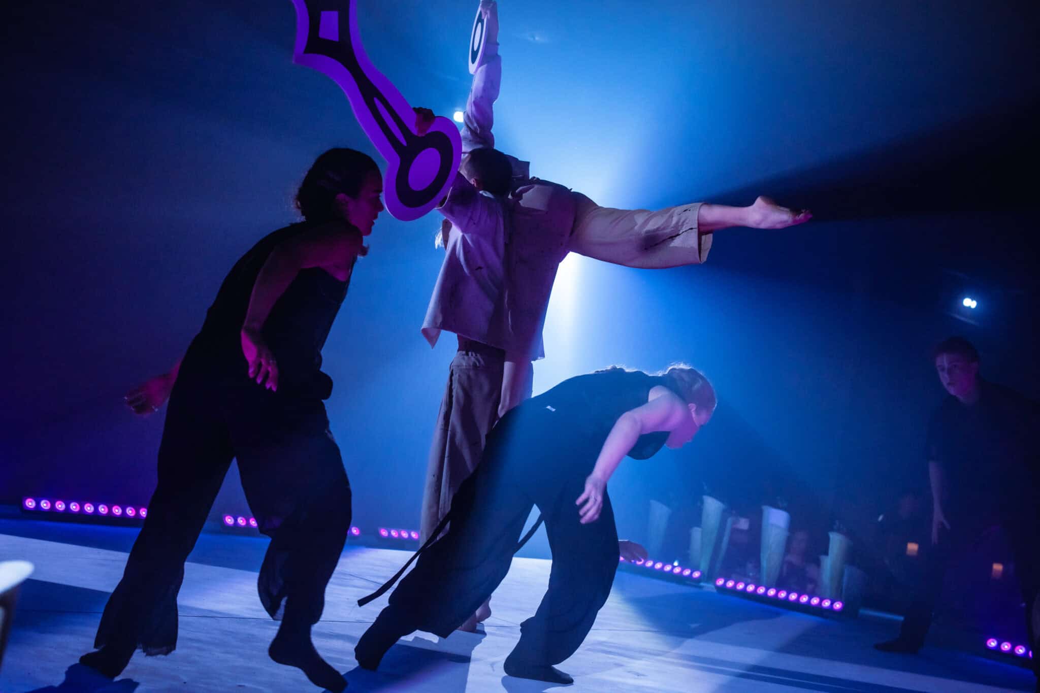 Dansers in een acrobatische voorstelling met kleurrijke belichting.