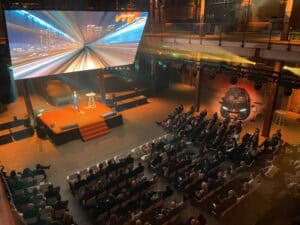 Congreszaal met groot scherm en publiek, ideaal voor zakelijke evenementen en presentaties.