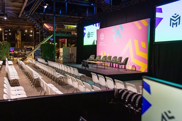 Congreszaal met podium, stoelen en grote schermen voor zakelijke bijeenkomsten.