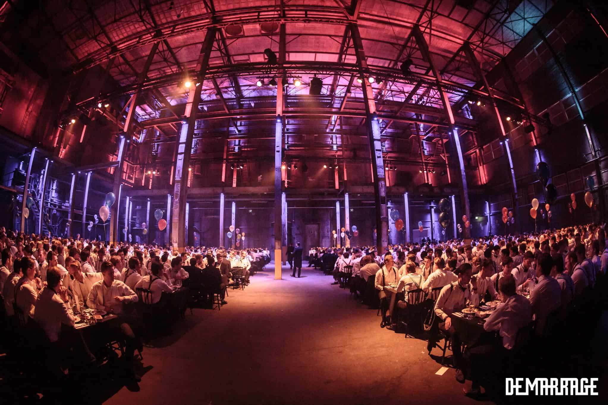 Groot diner met veel gasten in een industriële locatie met kleurrijk licht.