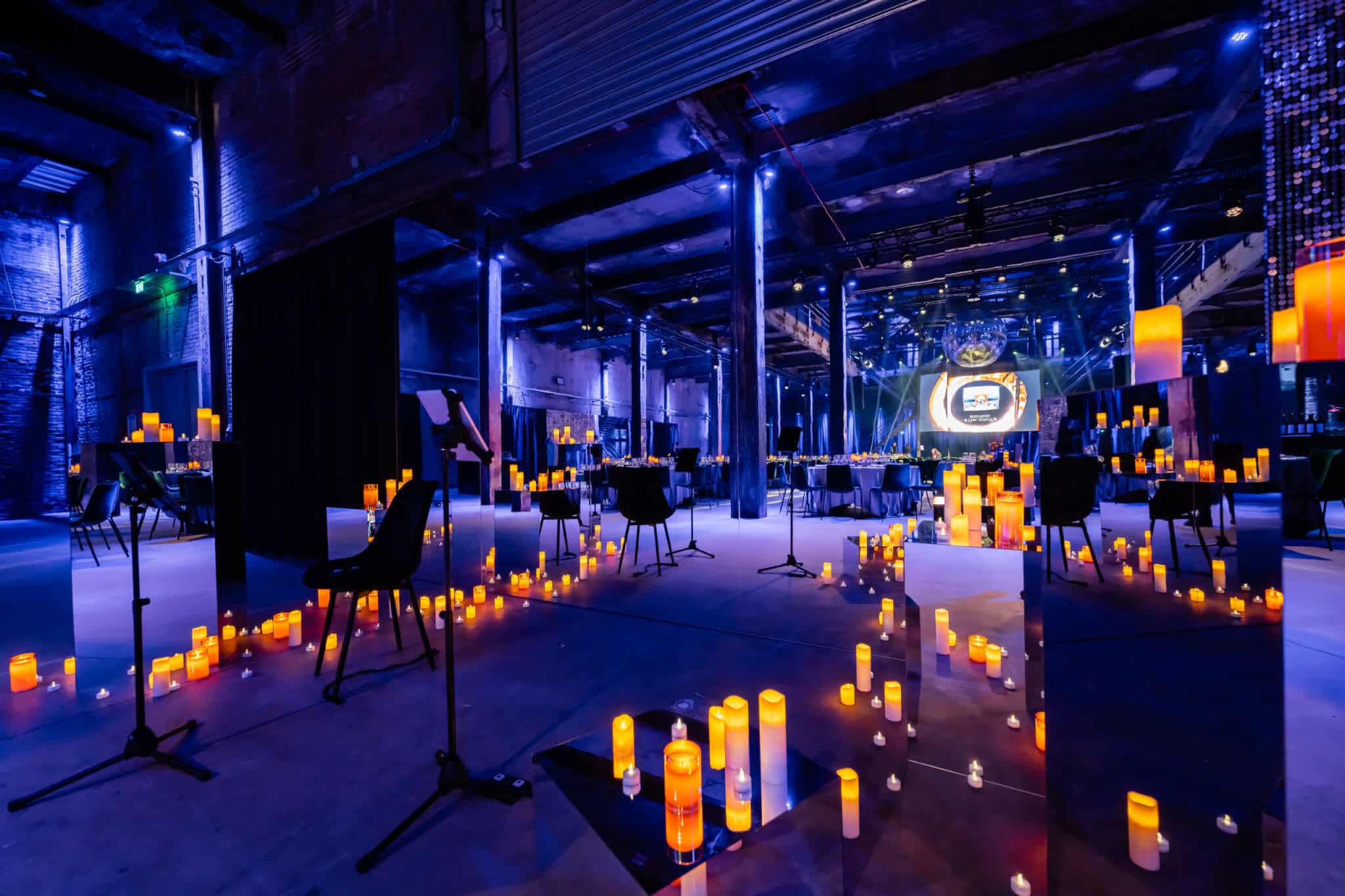 Awardshow setting met kaarsverlichting en podium in een industrieel gebouw.