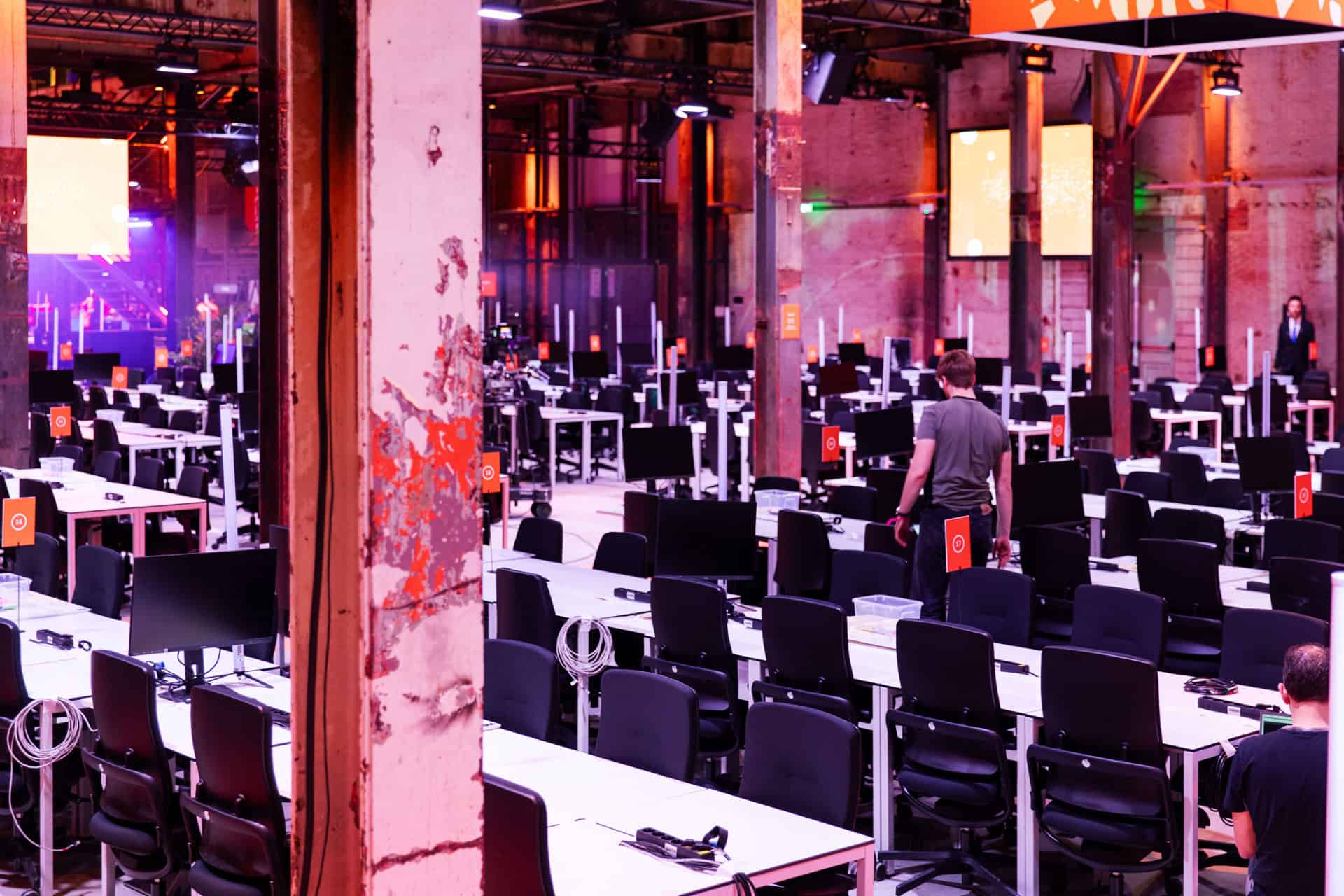 Grote industriële ruimte met opgestelde werkplekken voor hackathon.