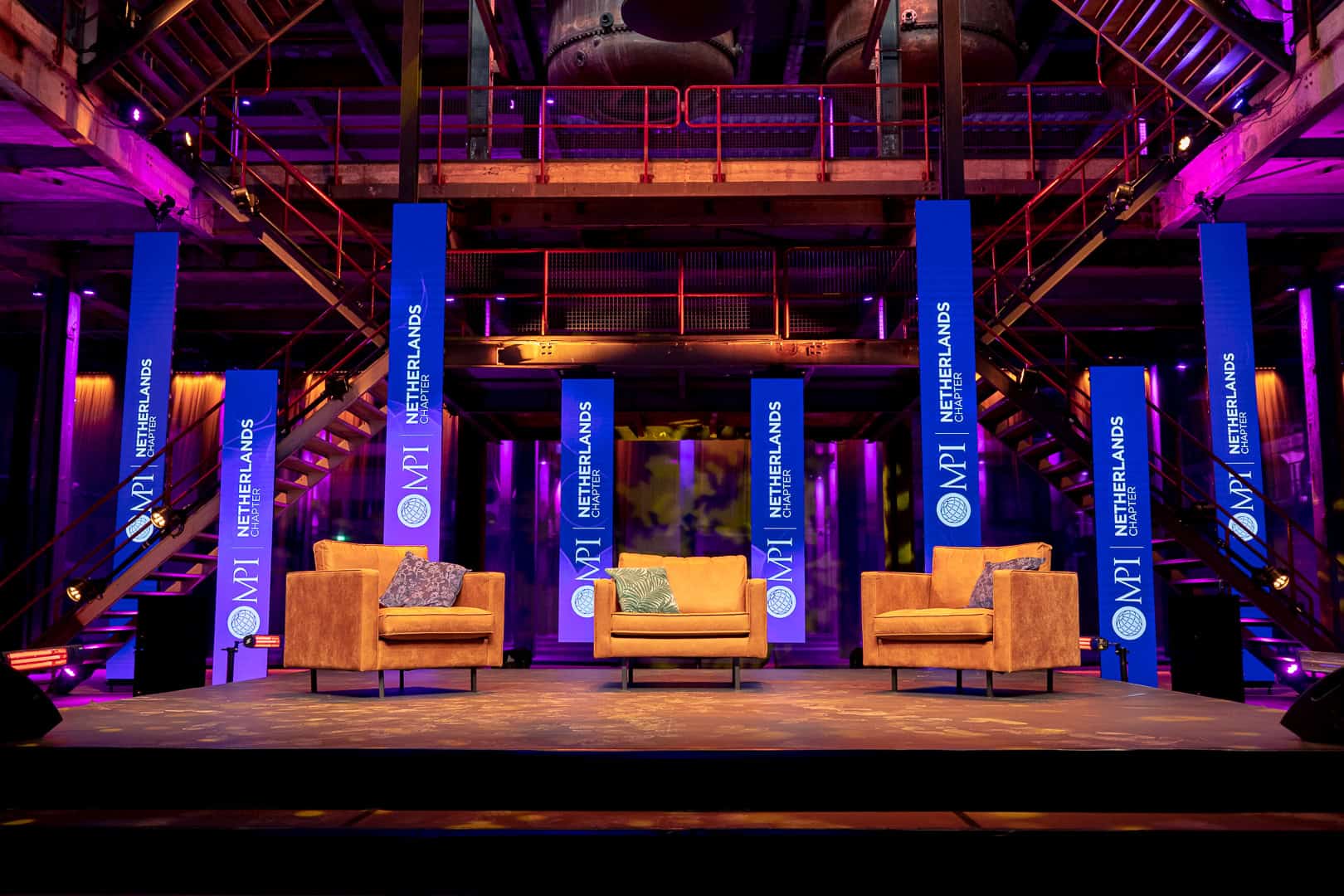 Moderne eventruimte met zitplaatsen en banners voor MPI Online Event.