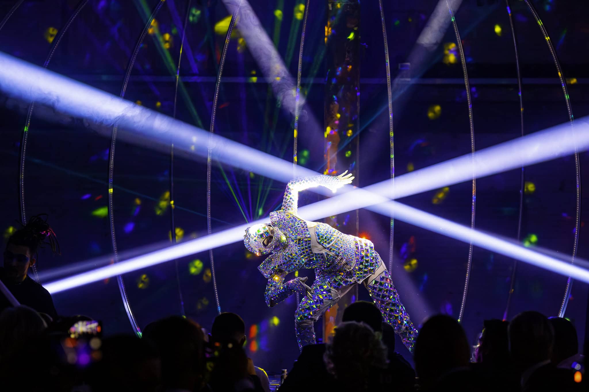 Danser in sprankelende kostuum met lichtshows op achtergrond.