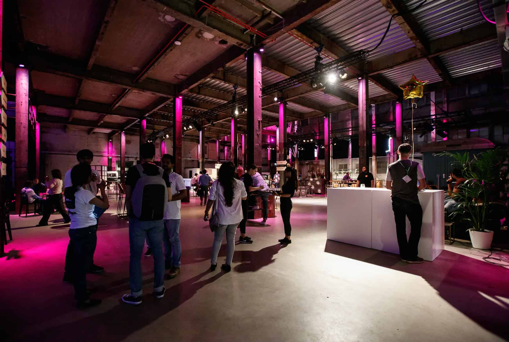 Bezoekers tijdens de Beyond Banking hackathon in SugarFactory, met kleurrijke verlichting en creatie.