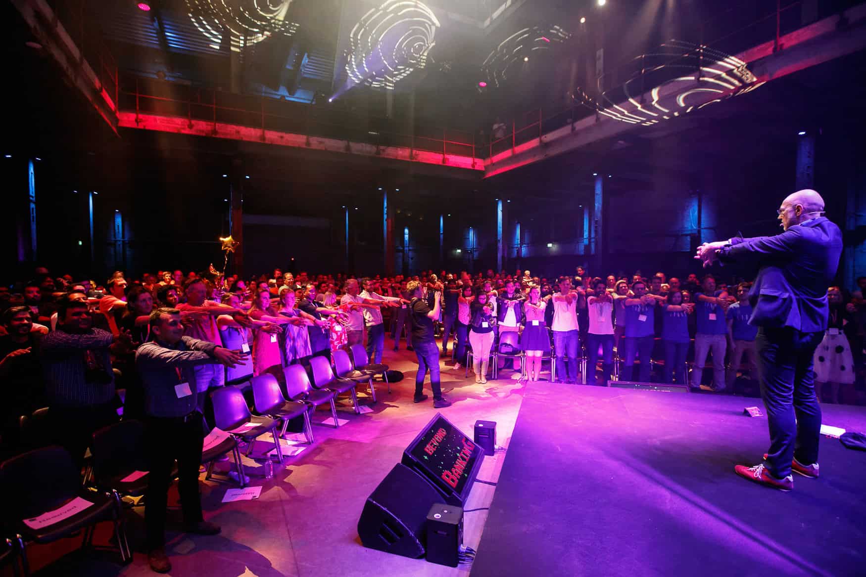 Spreker presenteert tijdens Beyond Banking hackathon in SugarFactory, omringd door deelnemers en tec.