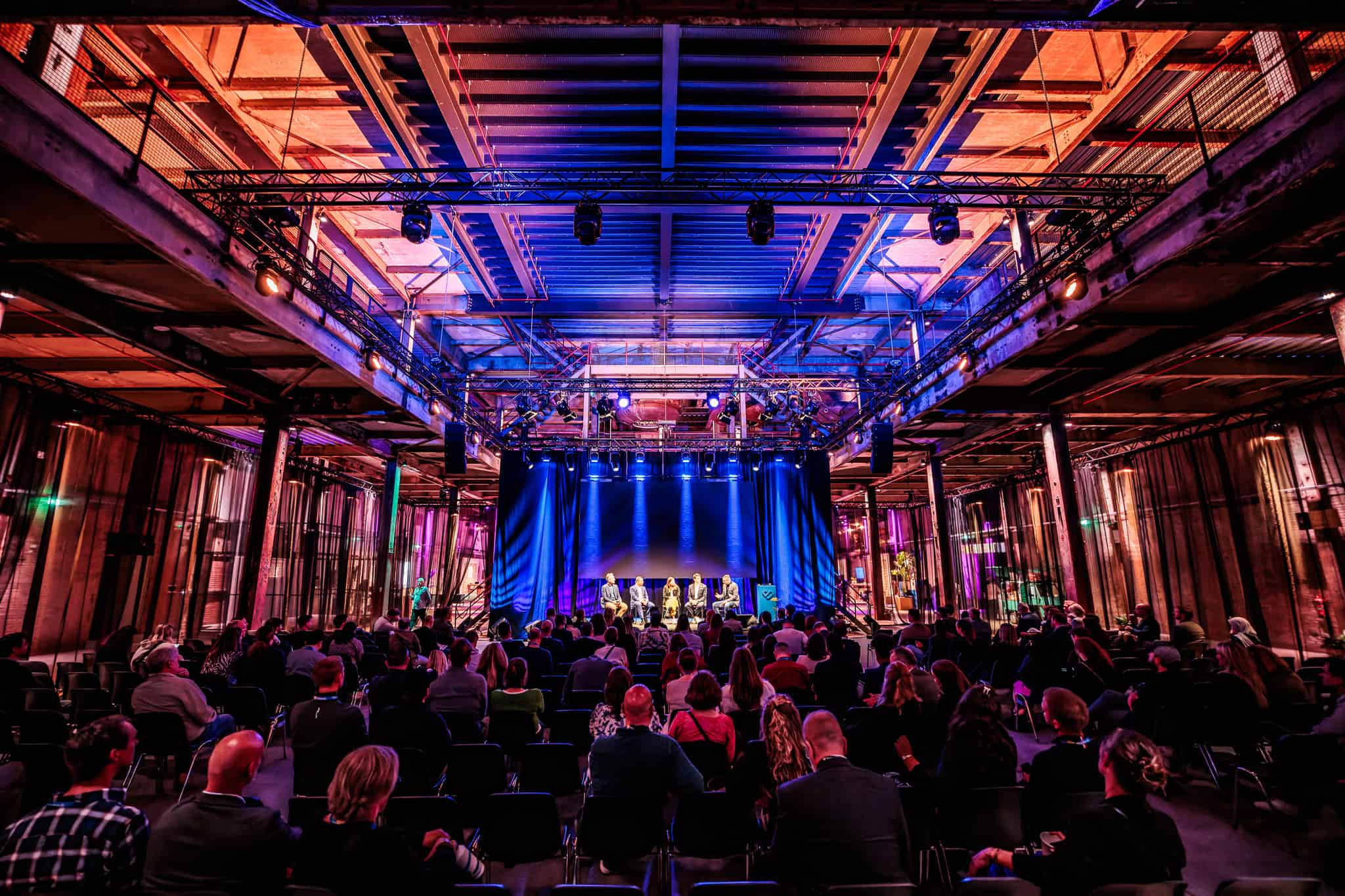 Groots congres in de industriële setting van SugarFactory met publiek en podium.