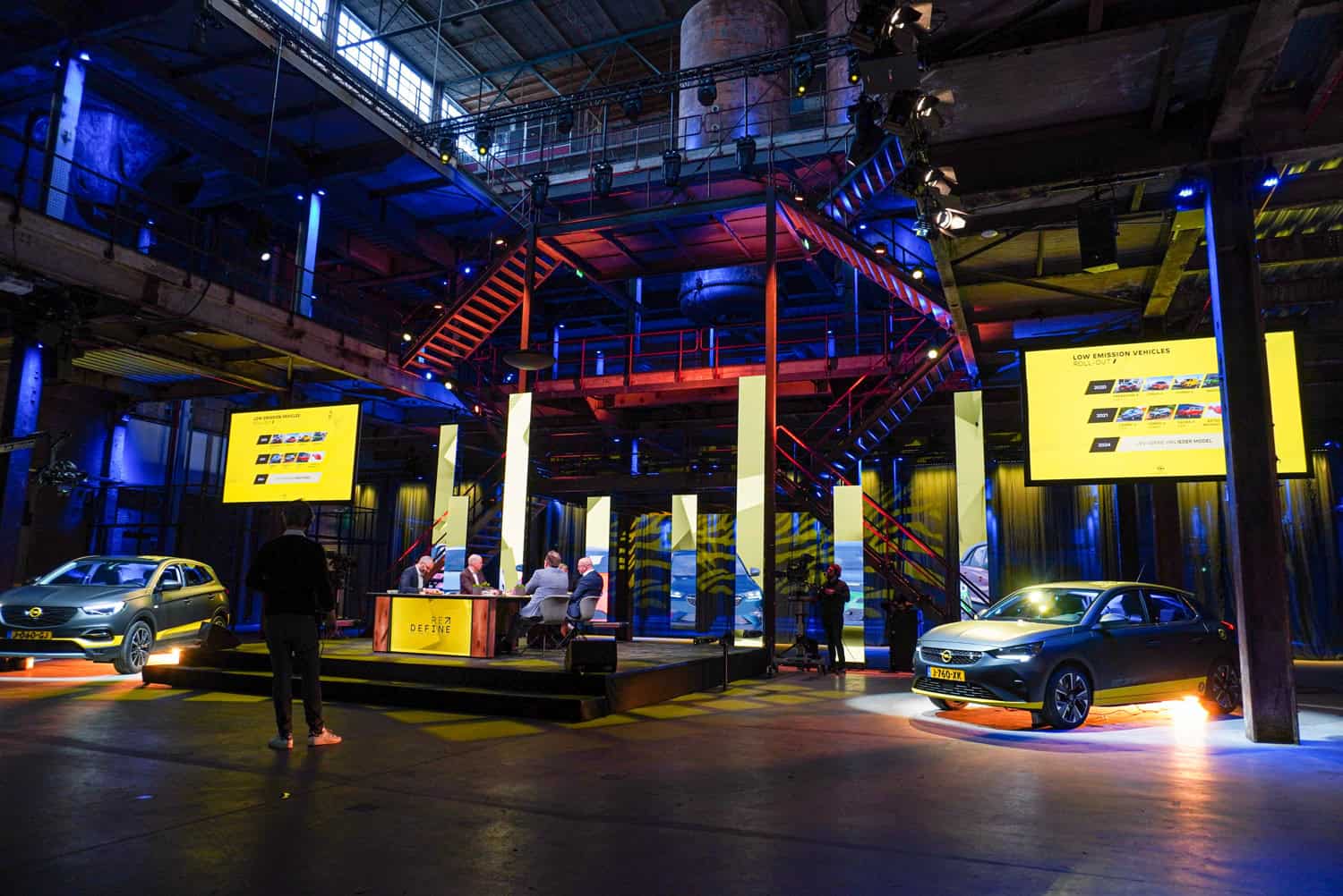 Opel Nederland strategiemeeting in een industrieel gebouw met auto's en presentatieschermen.