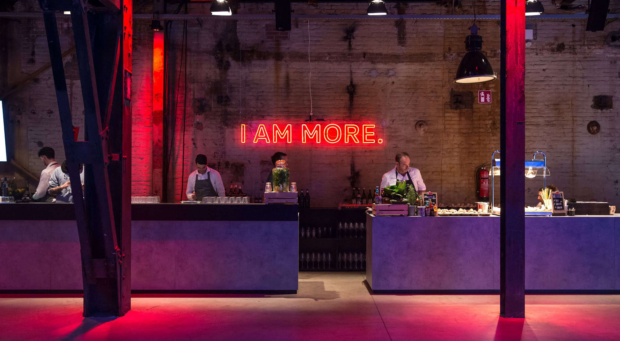 Binnenzicht van een bar met een neonbord "I AM MORE" in een industrieel interieur.