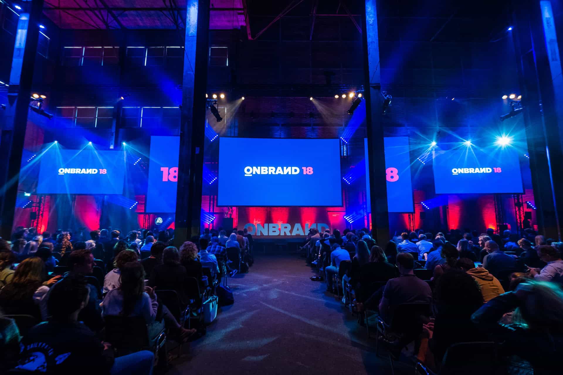 Evenementzaal tijdens OnBrand’18 bij SugarFactory met grote schermen en publiek.