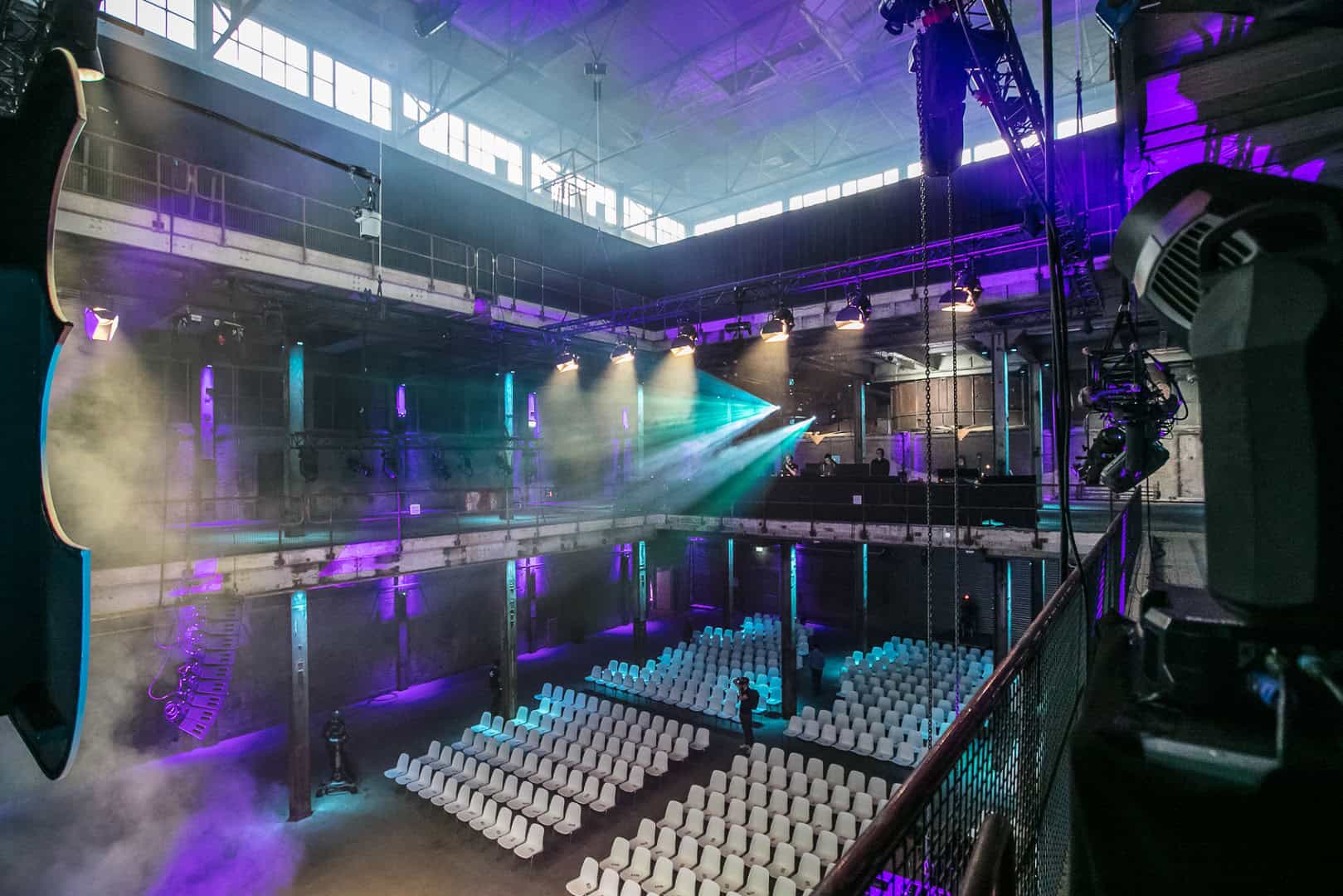 Evenementenhal met podium, zitplaatsen en kleurrijk licht voor optredens.
