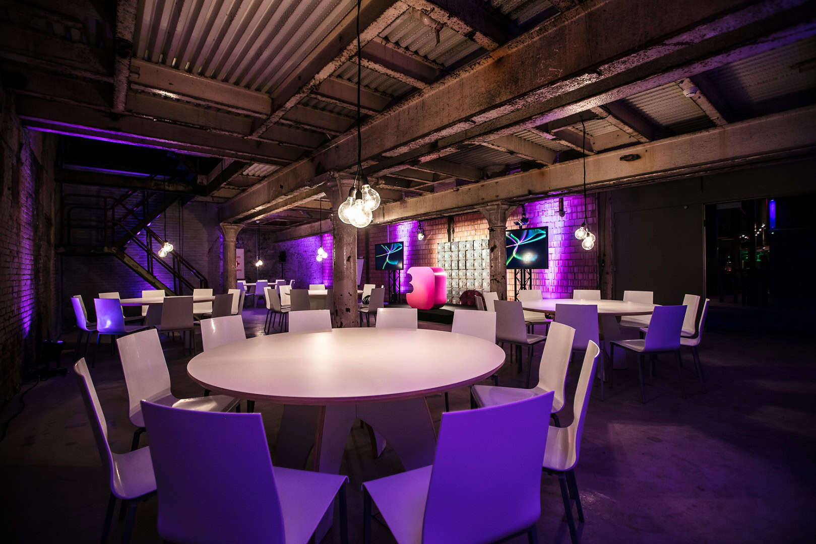 Moderne evenementenlocatie met industrieel design en kleurrijke verlichting.
