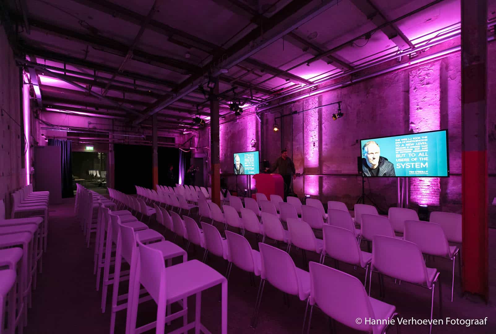 Moderne evenementenzaal met roze verlichting en rijen stoelen voor presentaties.