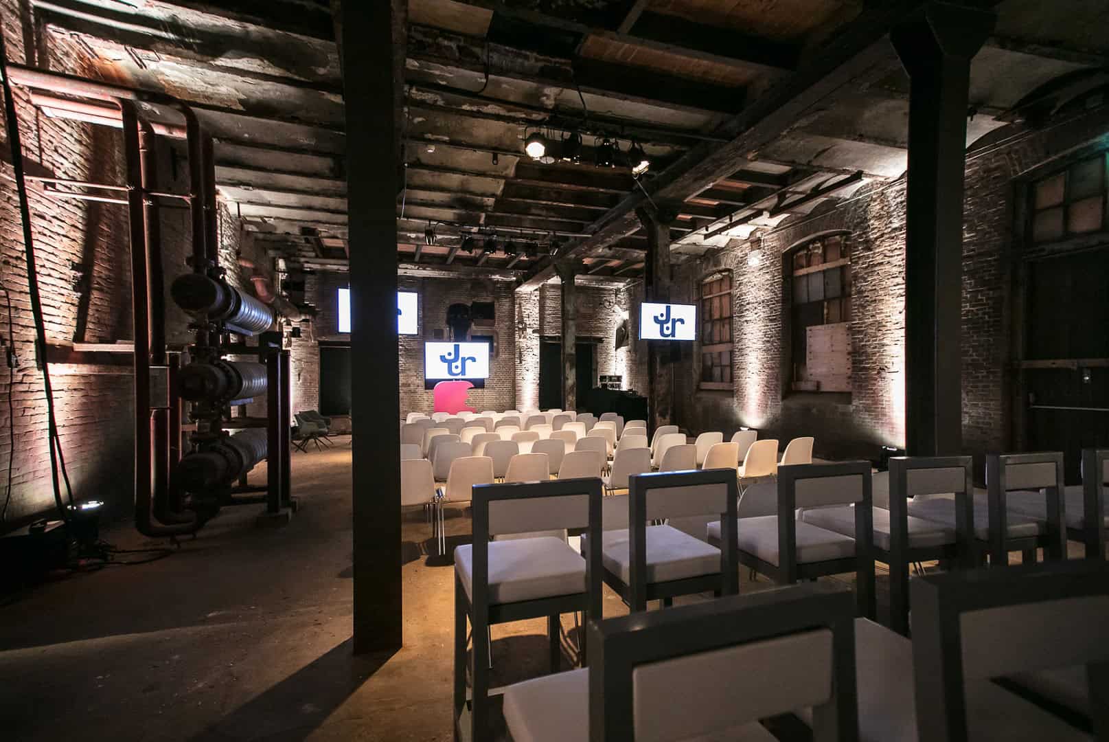 Vergaderruimte in een industrieel gebouw met stoelen en projectoren voor zakelijke presentaties.