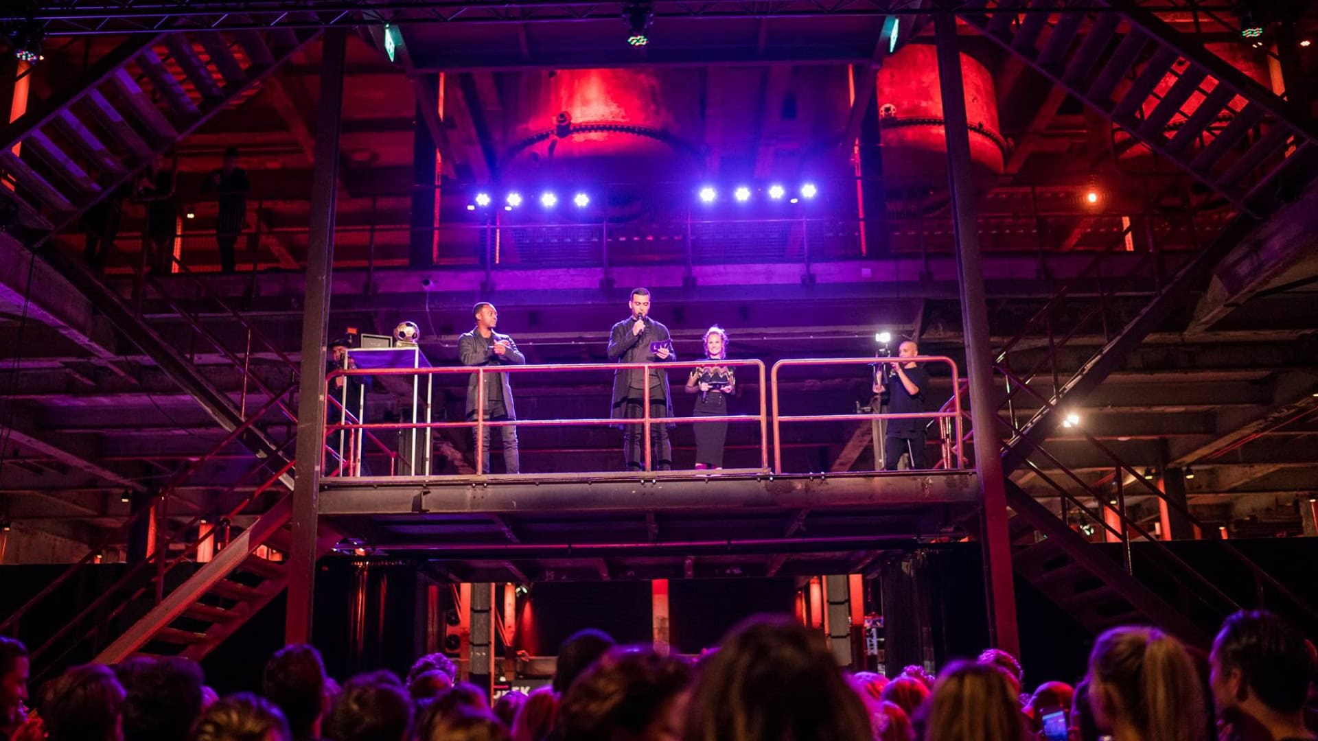 Drie mensen op een podium tijdens de Mode-Player Awards in een industrieel gebouw.