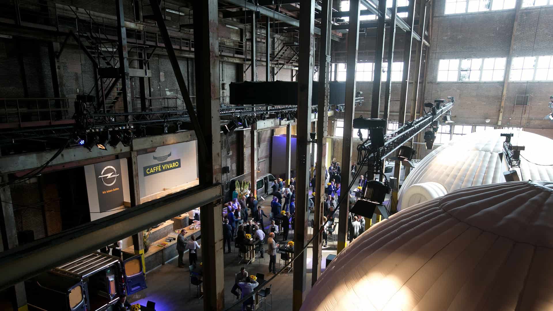 Opel auto in een grote industriële hal met mensen en apparatuur.