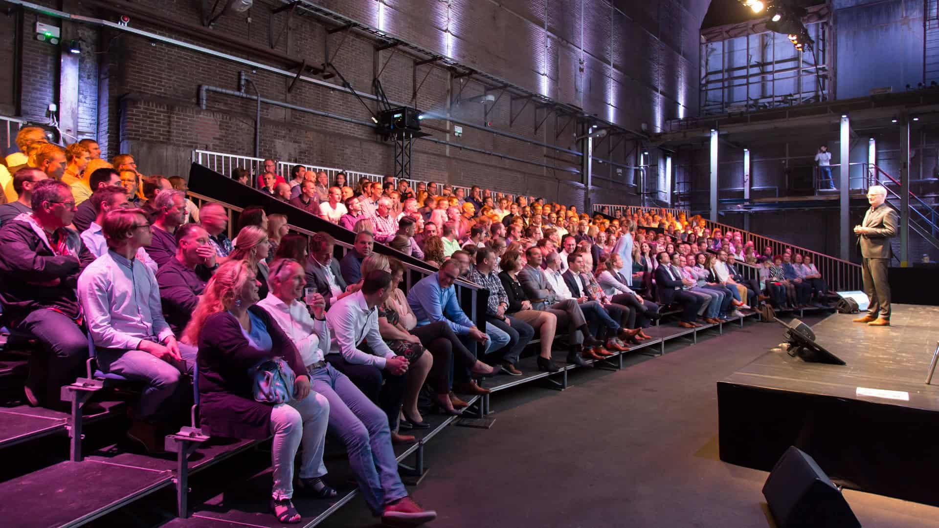 Publiek tijdens presentatie bij SugarFactory in een industrieel gebouw.
