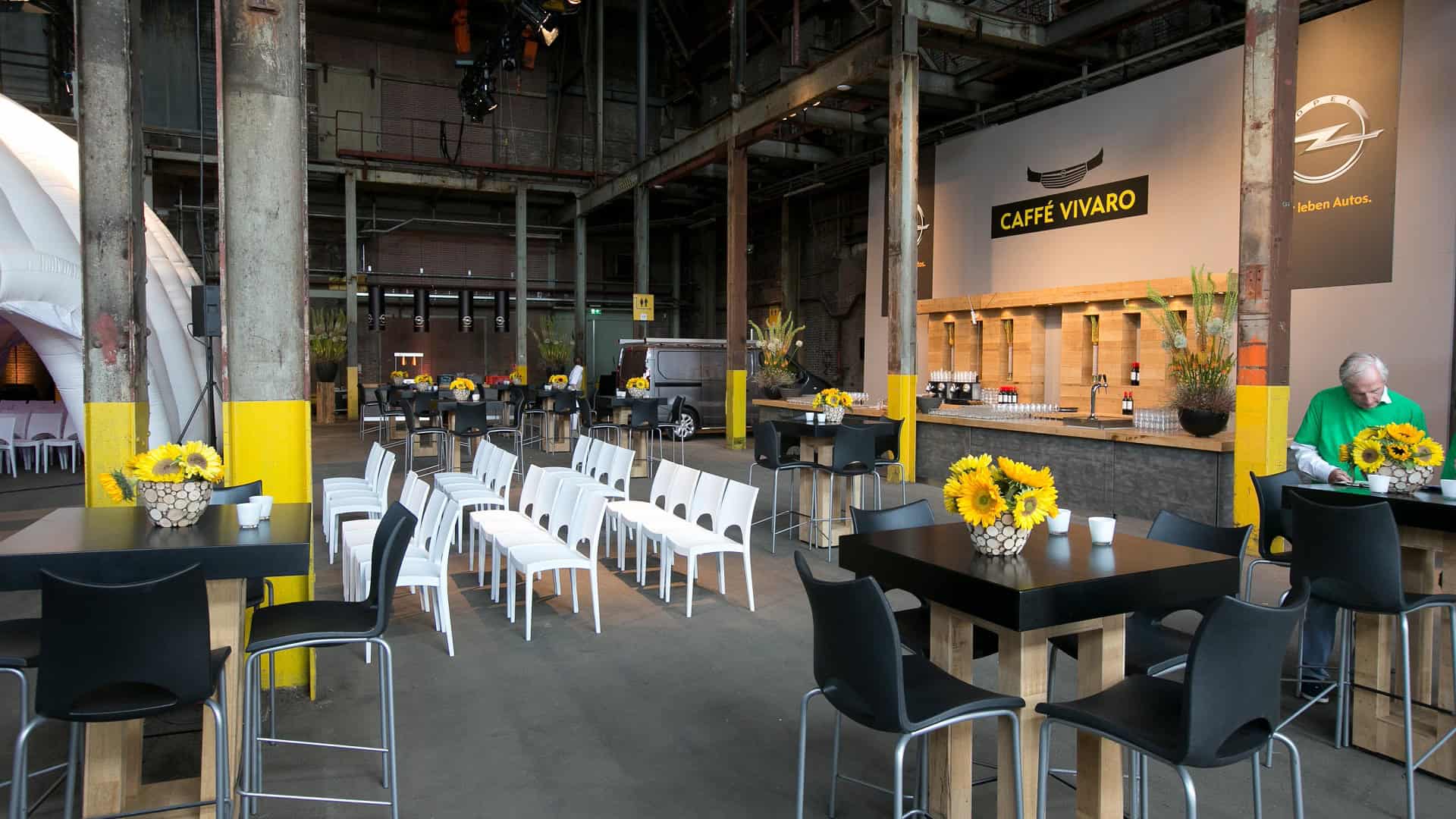 Auto van Opel in een industriële omgeving met stoelen en tafels.