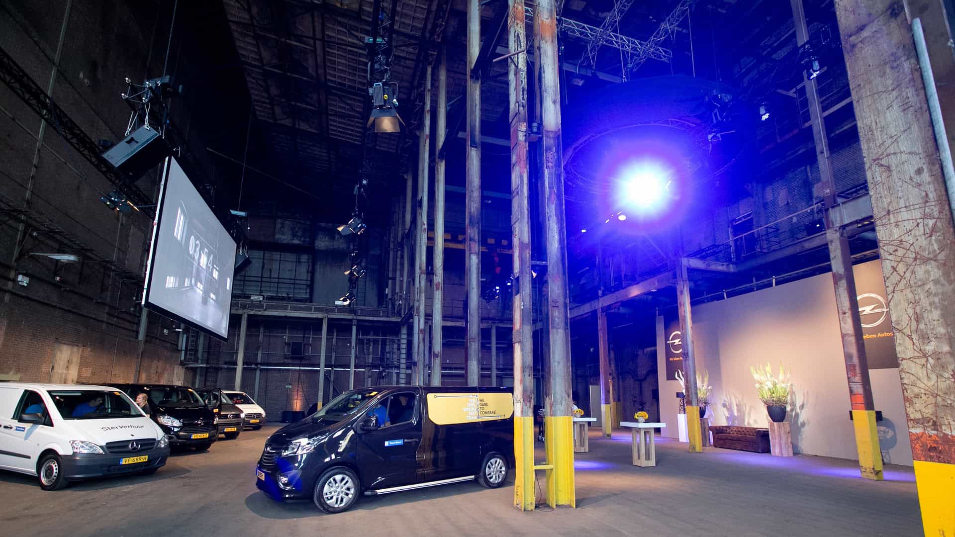 Een Opel auto geparkeerd in een industriële omgeving met hoge plafonds en metalen structuren.